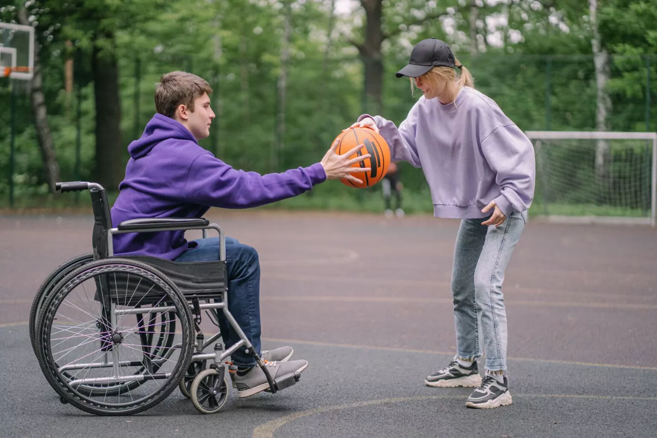 A woman passing a basketball to a man in a wheelchair on an outdoor court