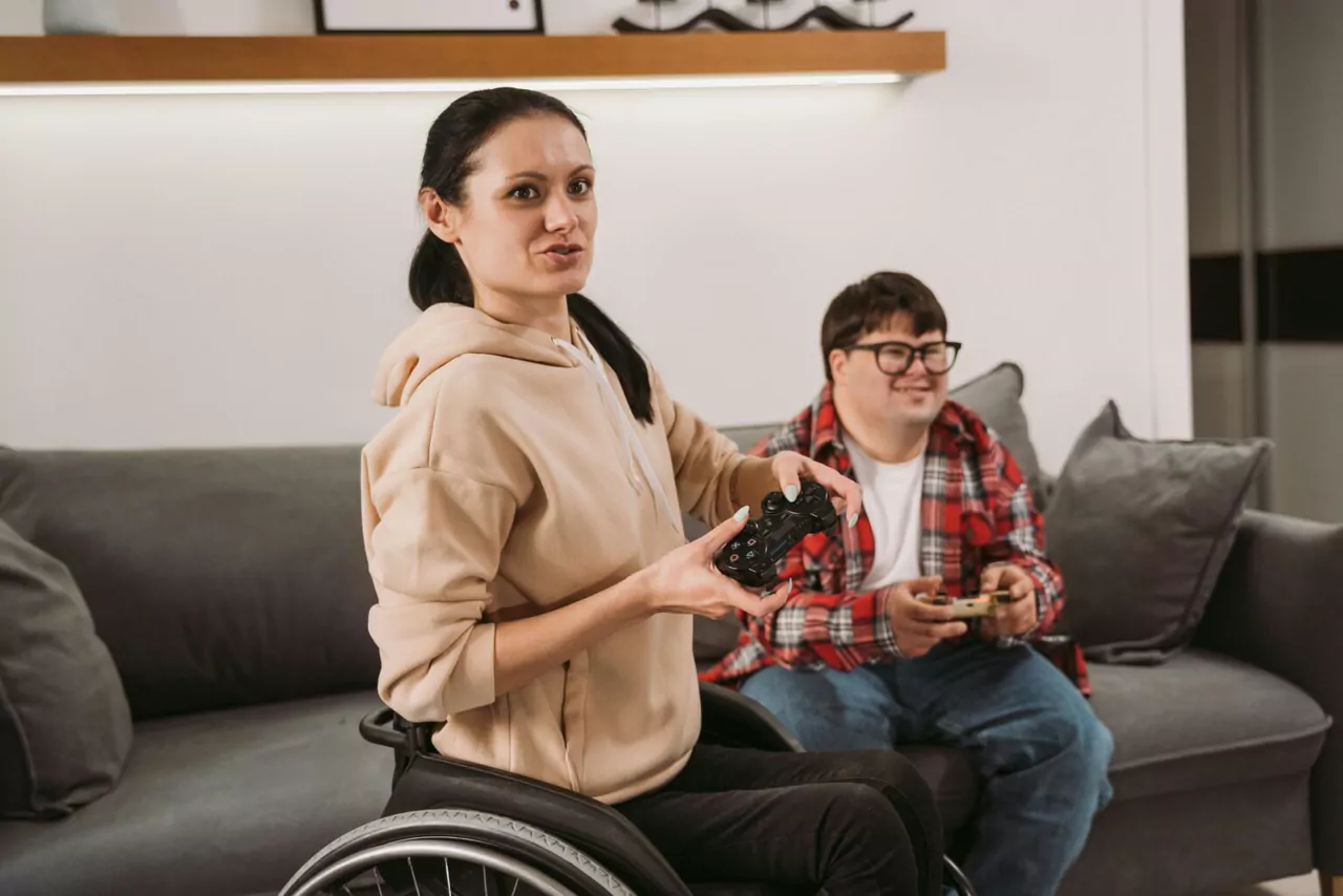 Two friends chatting on a couch at home, one of them using a wheelchair