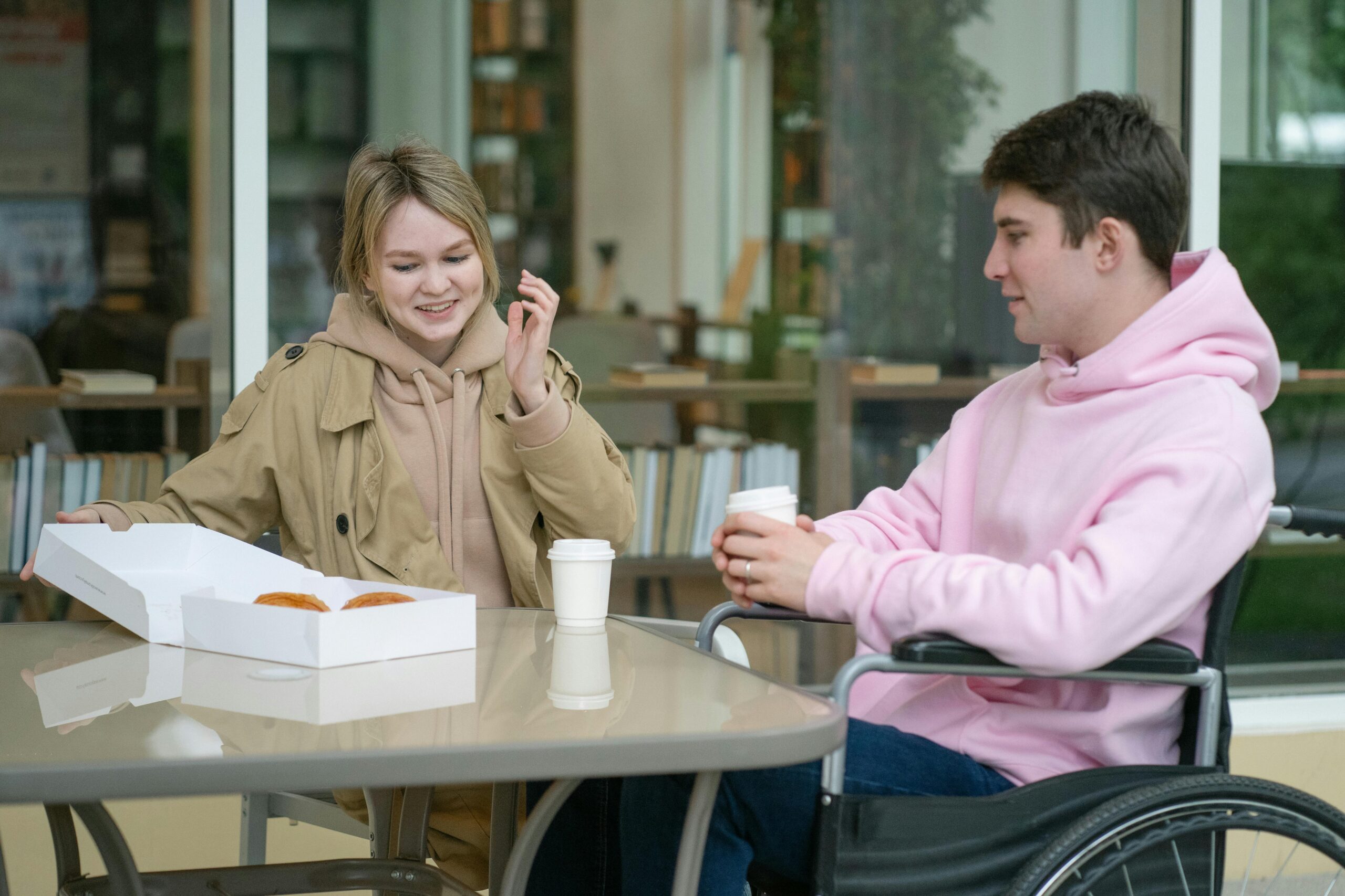A young man in a wheelchair sharing a meal with a friend at a cafe