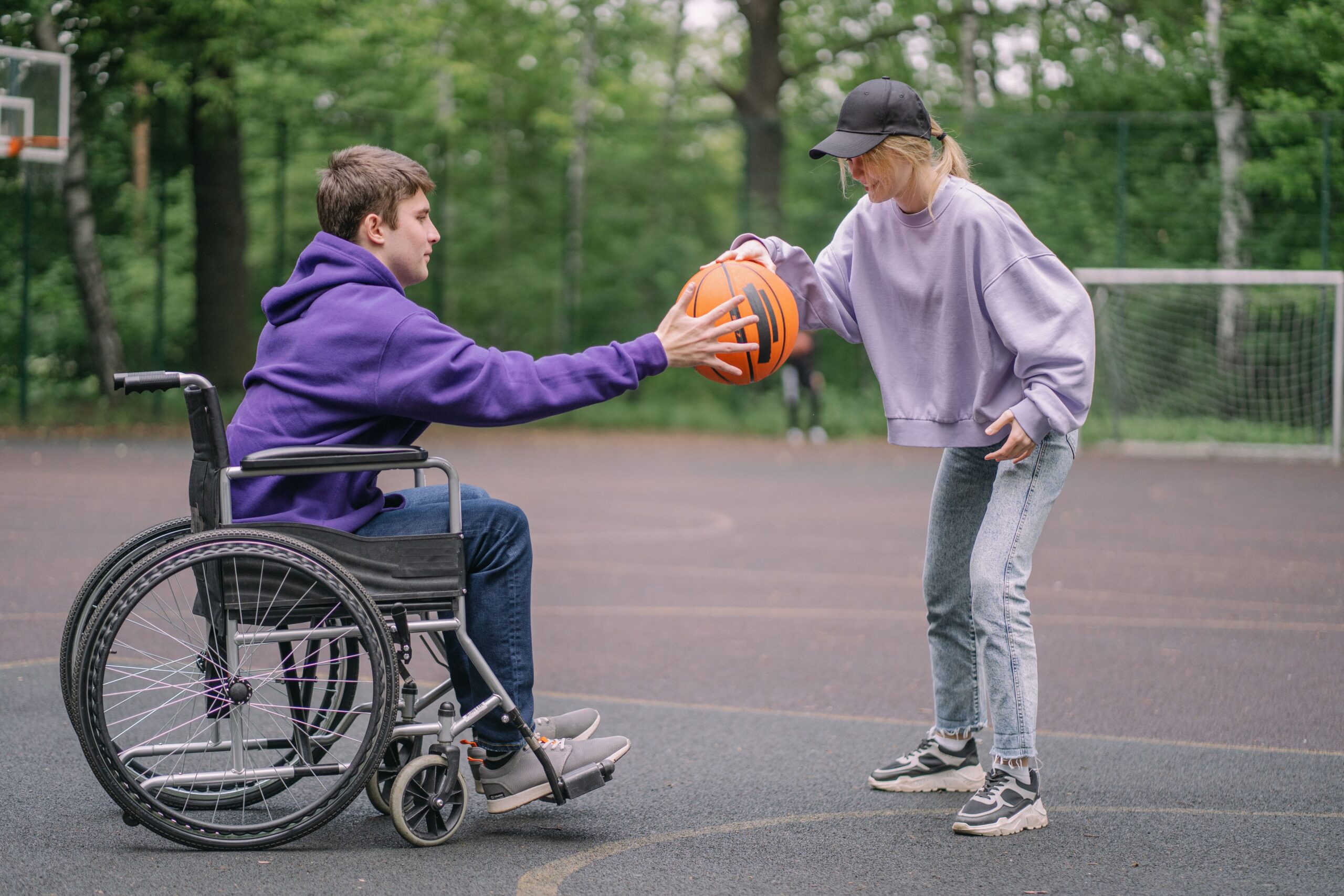 A woman passing a basketball to a man in a wheelchair on an outdoor court