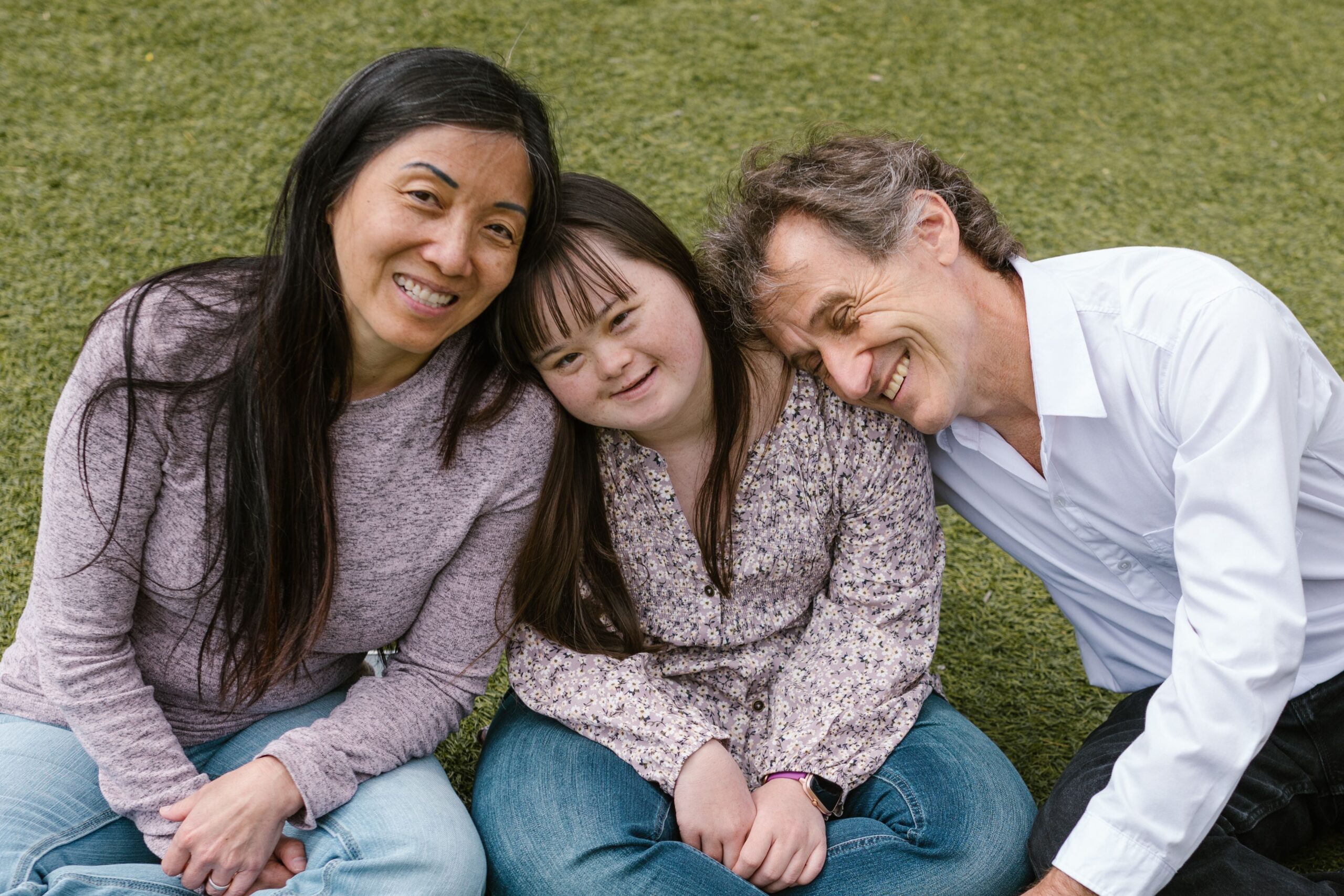 A young woman with Down syndrome laughing with her parents in a park
